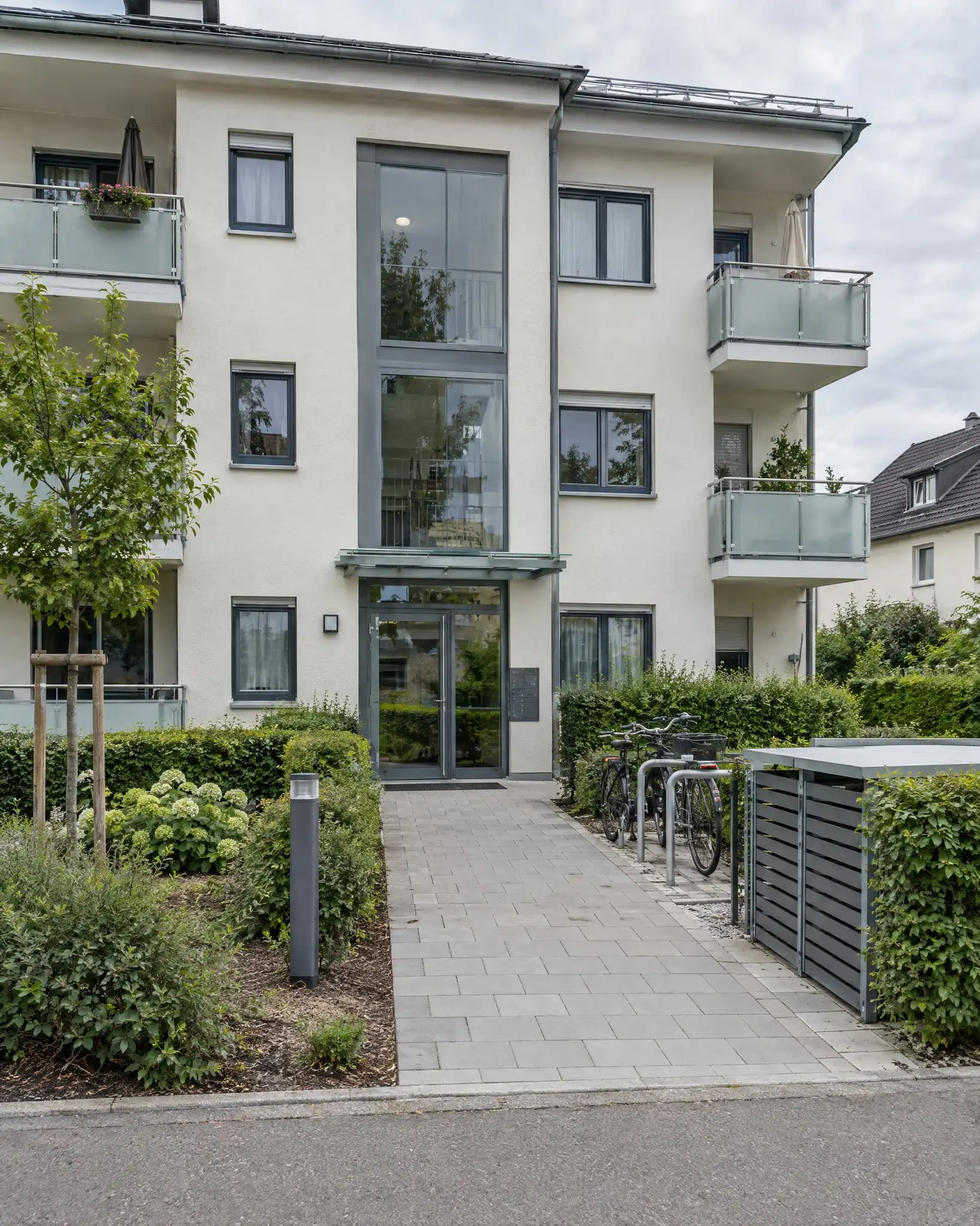 Gepflegtes Mehrfamilienhaus mit Balkonen, Hecken, Fahrradständern und Mülltonnenhaus